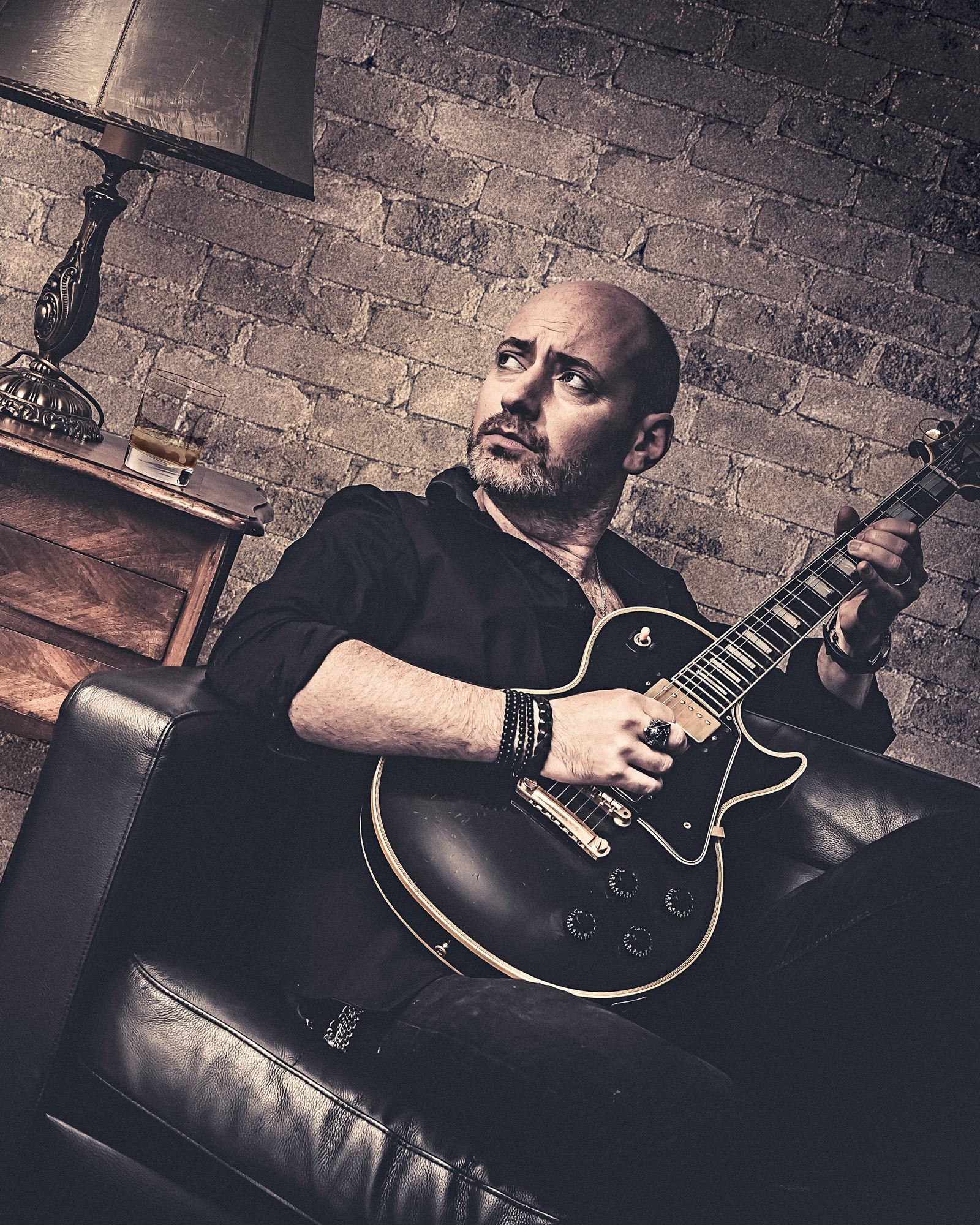Quentin Piepszownik avec une guitare électrique noire, devant un mur de briques.